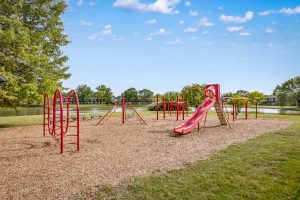 Children's play park with slide, woodchips, and benches with lake in background