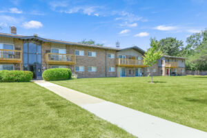 Exterior brick Residential buildings, large field of grass, Sidewalk leading to building, meticulous landscaping, lush foliage, photo taken a sunny day.