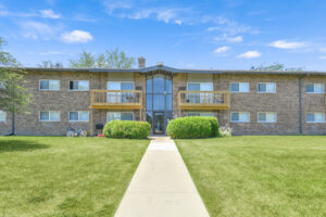 Exterior brick Residential buildings, large field of grass, Sidewalk leading to building, meticulous landscaping, lush foliage, photo taken a sunny day.