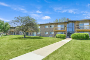 Exterior brick Residential buildings, large field of grass, Sidewalk leading to building, meticulous landscaping, lush foliage, photo taken a sunny day.