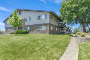 Exterior brick Residential buildings, large field of grass, Sidewalk leading to building, meticulous landscaping, lush foliage, photo taken a sunny day.