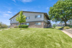 Exterior brick Residential buildings, large field of grass, Sidewalk leading to building, meticulous landscaping, lush foliage, photo taken a sunny day.