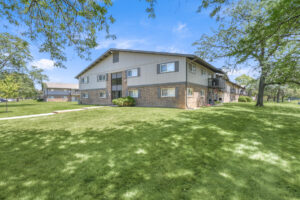 Exterior brick Residential buildings, large field of grass, Sidewalk leading to building, meticulous landscaping, lush foliage, photo taken a sunny day.