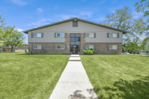 Exterior brick Residential buildings, large field of grass, Sidewalk leading to building, meticulous landscaping, lush foliage, photo taken a sunny day.