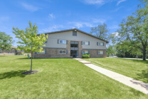 Exterior brick Residential buildings, large field of grass, Sidewalk leading to building, meticulous landscaping, lush foliage, photo taken a sunny day.