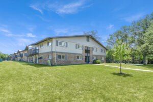 Exterior brick Residential buildings, large field of grass, Sidewalk leading to building, meticulous landscaping, lush foliage, photo taken a sunny day.