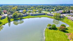 Aerial Exterior of Body of water in Acclaim at Hinsdale Lake, Meticulous Landscaping, Lush Foliage, Treeline in the distance, Photo taken on a sunny day.