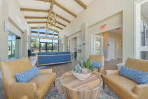 Interior Clubhouse, contemporary rustic decor, multiple seated areas, wood floors, large glass windows, high ceilings.