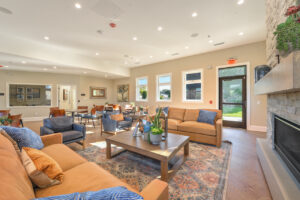 Interior Clubhouse Lounge area, 2 large couches, 2 lounge chairs, contemporary rustic decor, stone fireplace, abstract art on the walls, wood floors.