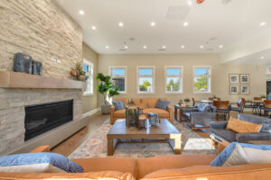 Interior Clubhouse Lounge area, 2 large couches, 2 lounge chairs, contemporary rustic decor, stone fireplace, abstract art on the walls, wood floors.