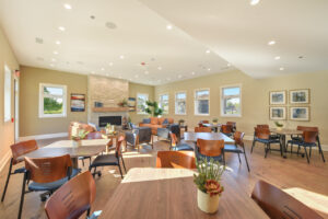 Interior Clubhouse, dining area, multiple bistro dining tables, lounge area in back of room, couches, lounge chairs.