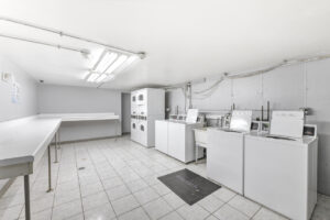 Interior Laundry Facilities, tile floor, white walls, large table running around the perimeter of the room for folding, four washers four dryers.