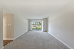 Interior Unit Living room, Neutral toned walls and carpeting, wood floors in the hallway, sliding glass doors to balcony .