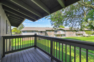 Exterior Unit Balcony, wood decking, wood railing, view of lush foliage, large grass fields, photo taken on a sunny day.