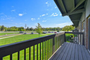Exterior Unit Balcony, Wood decking, wood railing, view of lush foliage, large grass fields, tree line in the distance, photo taken on a sunny day.