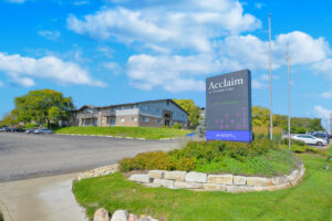 Exterior Front Signage, meticulous landscaping, residential building in the background, lush foliage, photo taken on a sunny day.