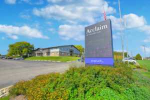 Exterior Front Signage, meticulous landscaping, residential building in the background, lush foliage, photo taken on a sunny day.